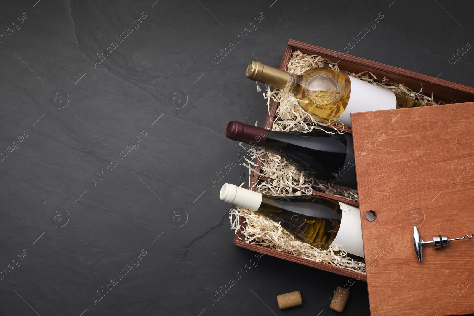 Photo of Box with wine bottles, corkscrew and corks on dark textured table, flat lay. Space for text