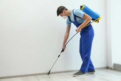 Pest control worker spraying pesticide in room. Space for text