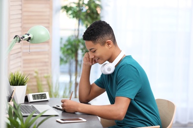 Photo of African-American teenage boy doing homework at table in room