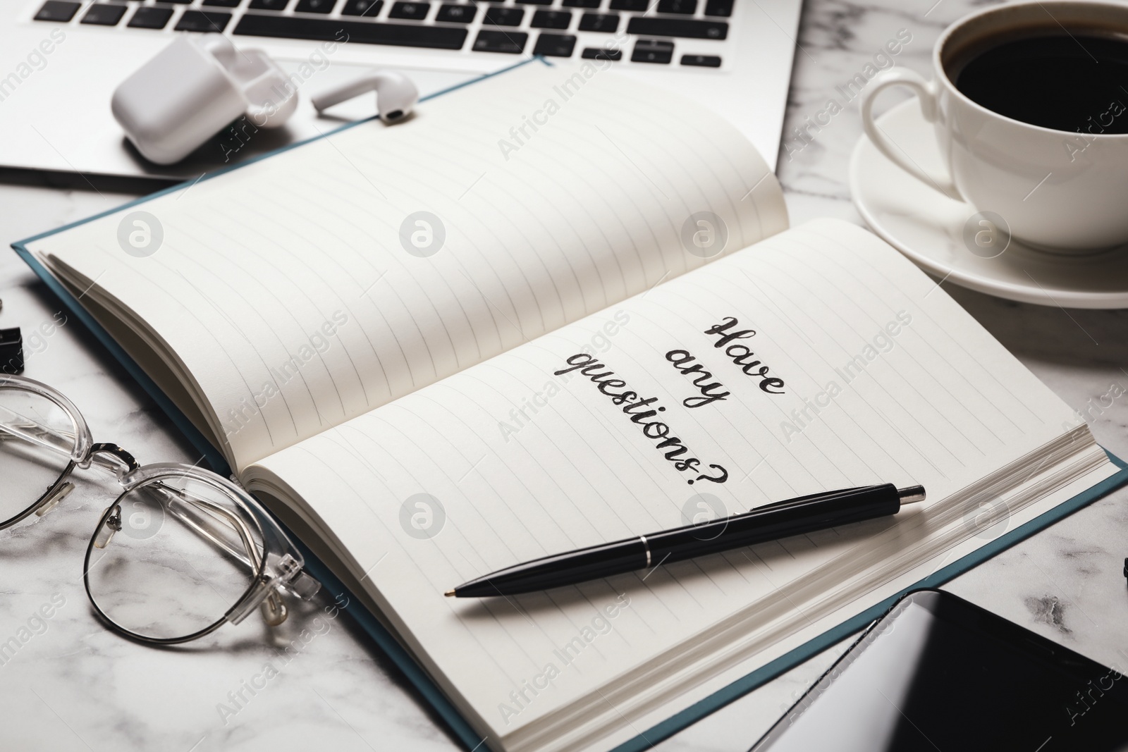 Photo of Notebook with phrase HAVE ANY QUESTIONS on white marble table
