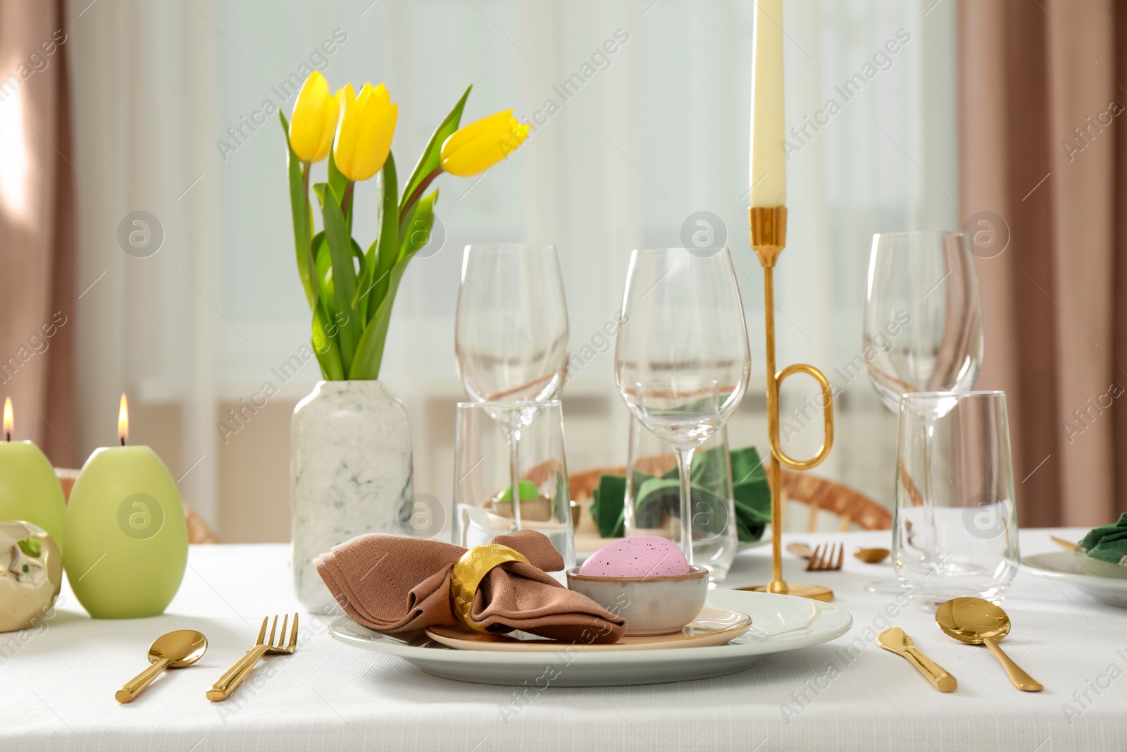 Photo of Festive Easter table setting with painted egg, burning candles and yellow tulips indoors