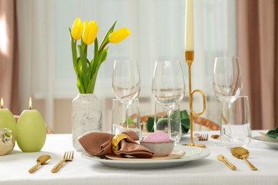 Festive Easter table setting with painted egg, burning candles and yellow tulips indoors