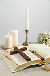 Church candles, wooden cross, rosary beads, Bible and flowers on light table