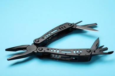 Photo of Compact portable black multitool on light blue background, closeup