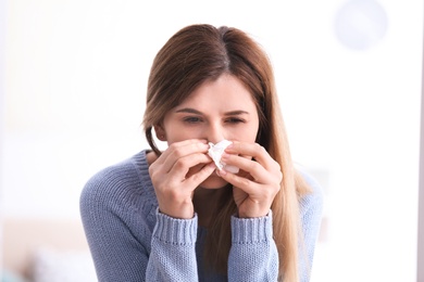 Photo of Sad woman with tissue suffering from cold on blurred background