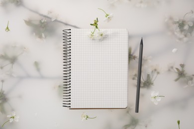 Photo of Guest list. Notebook, pencil and beautiful cherry tree blossoms on spring floral background, flat lay