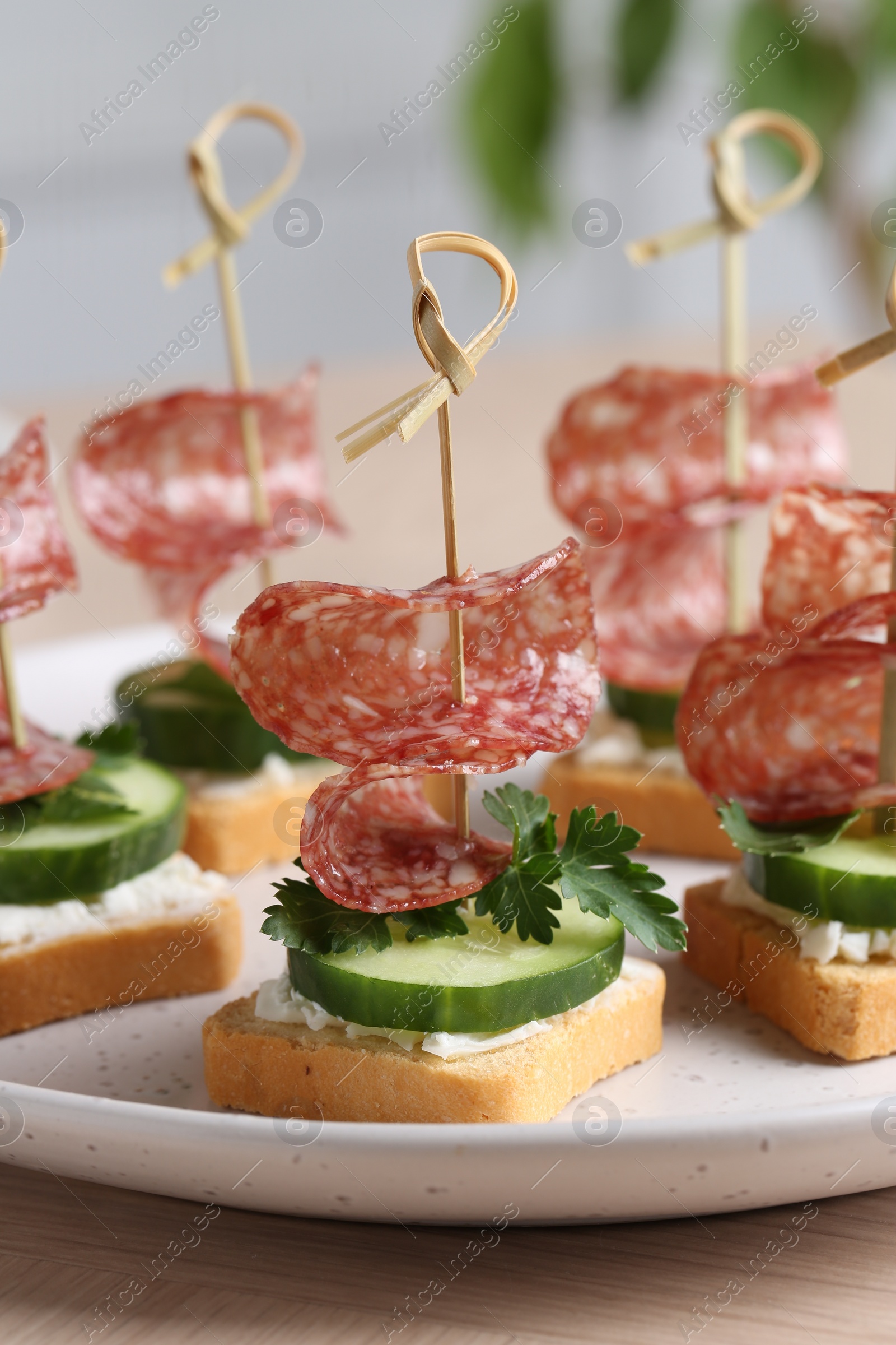 Photo of Tasty canapes with salami, cucumber and cream cheese on light table, closeup