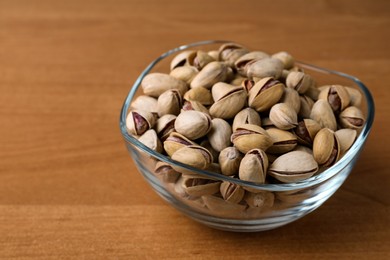 Photo of Bowl with pistachio nuts on wooden table, space for text