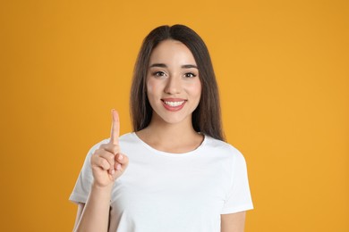 Woman in white t-shirt showing number one with her hand on yellow background