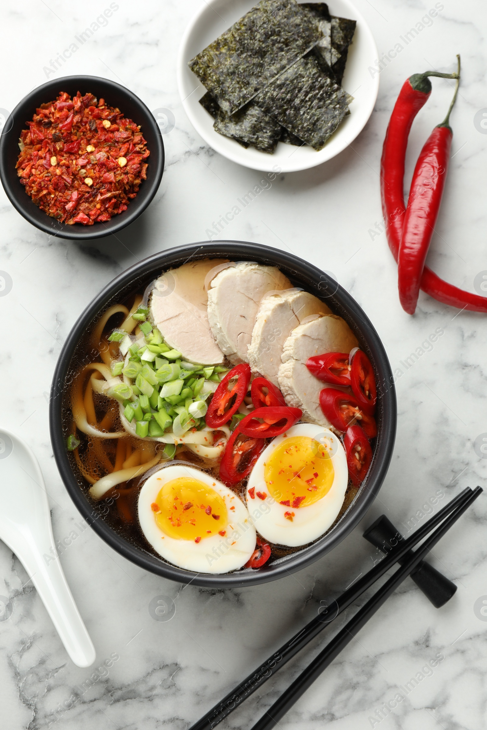 Photo of Delicious ramen in bowl served on white marble table, flat lay. Noodle soup