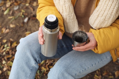 Woman with thermos sitting on ground outdoors, closeup