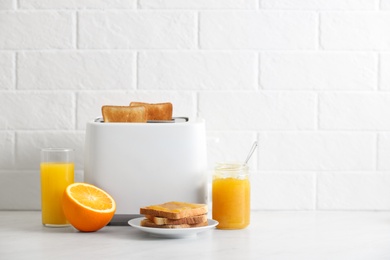 Photo of Modern toaster and delicious breakfast on table near brick wall. Space for text