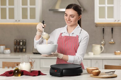 Photo of Young woman cooking delicious crepes in kitchen