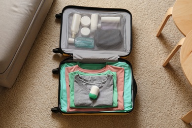 Photo of Deodorant in packed suitcase on floor indoors, top view