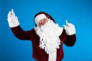 Photo of Santa Claus with headphones listening to Christmas music on blue background