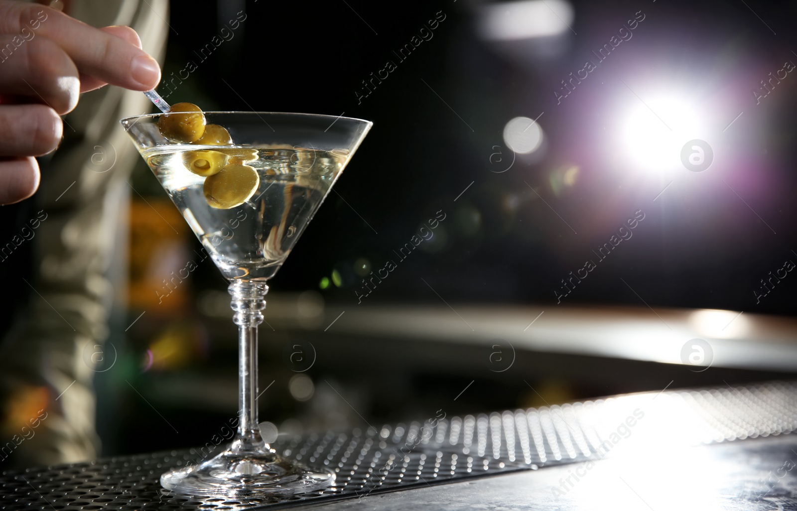 Photo of Barman adding olives to martini cocktail on counter, closeup. Space for text