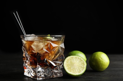 Photo of Glass of cocktail with cola, ice and cut lime on table against black background. Space for text