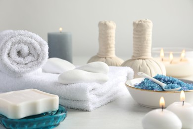 Photo of Spa composition. Towels, herbal bags, soap, sea salt and burning candles on light table