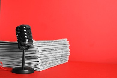 Photo of Newspapers and vintage microphone on red background, space for text. Journalist's work