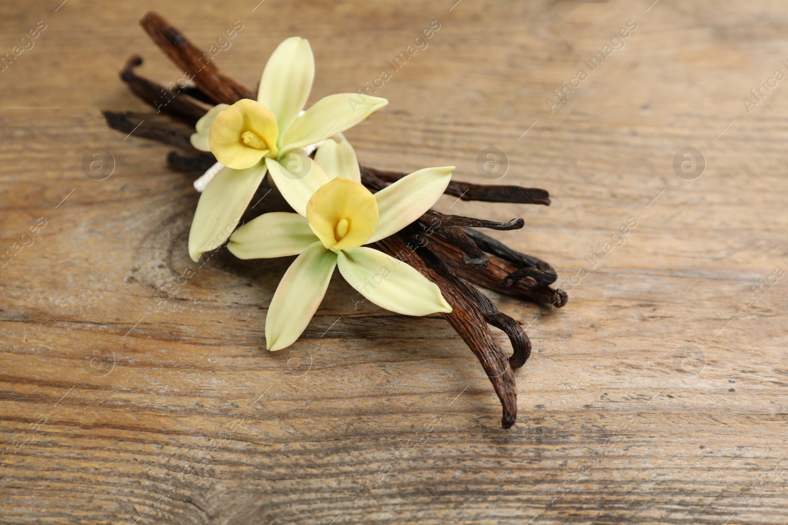 Photo of Aromatic vanilla sticks and flowers on wooden table, closeup