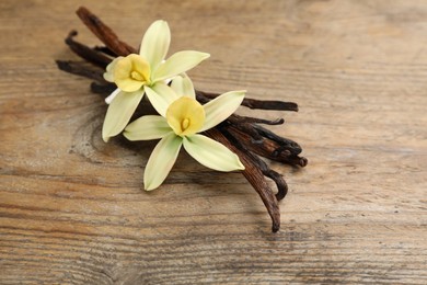 Aromatic vanilla sticks and flowers on wooden table, closeup