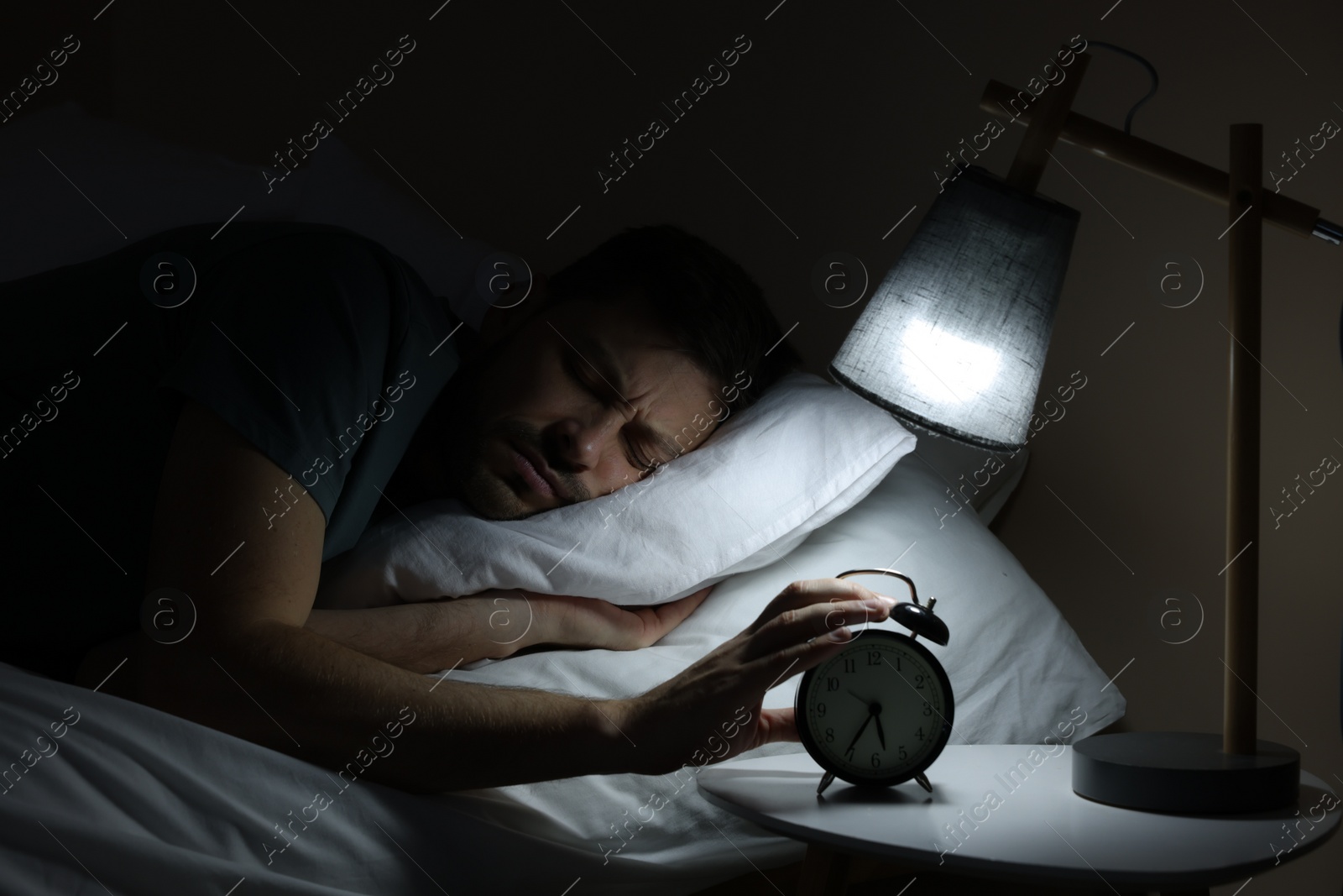 Photo of Sleepy man turning off alarm clock on nightstand in morning