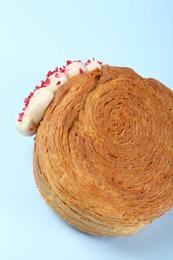 Photo of One supreme croissant with cream on light blue background, closeup. Tasty puff pastry