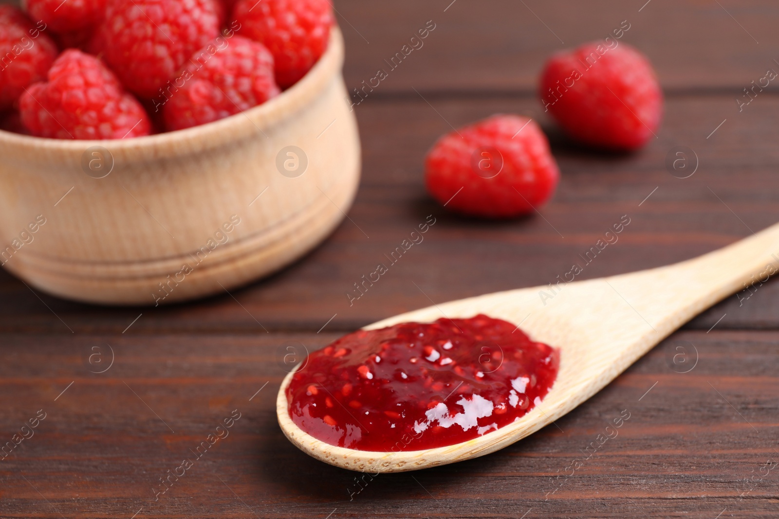 Photo of Jam in spoon and fresh raspberries on wooden table, closeup