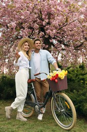 Lovely couple with bicycle and flowers in park on pleasant spring day