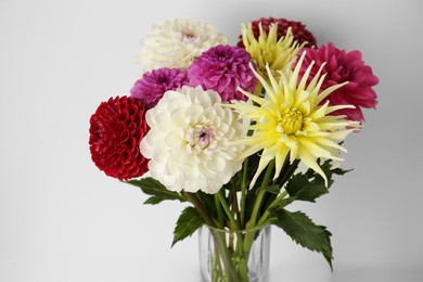 Photo of Bouquet of beautiful Dahlia flowers in vase near white wall, closeup