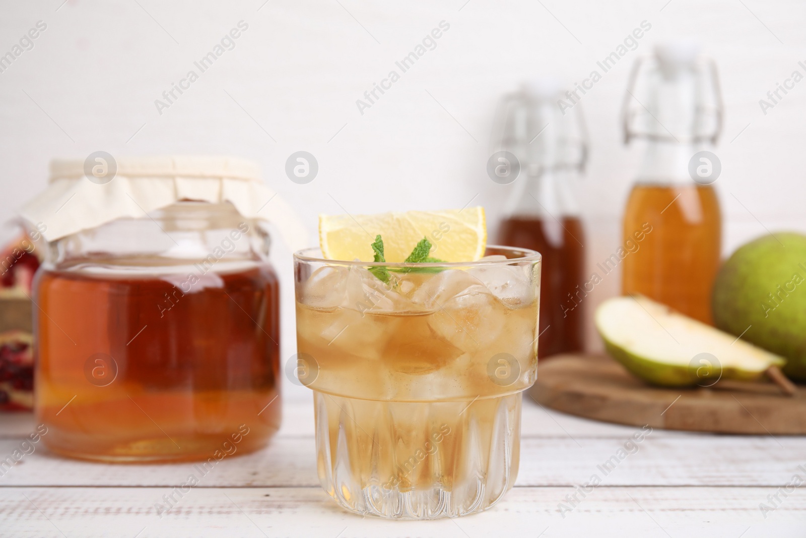 Photo of Tasty kombucha and ice cubes in glass on white wooden table
