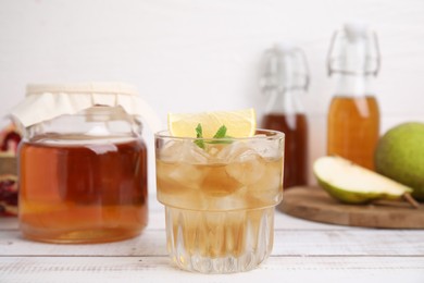 Tasty kombucha and ice cubes in glass on white wooden table