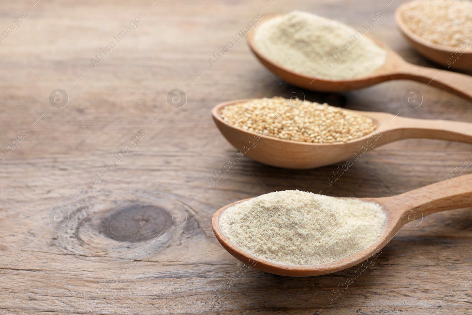 Photo of Spoons with quinoa flour and seeds on wooden table, closeup. Space for text