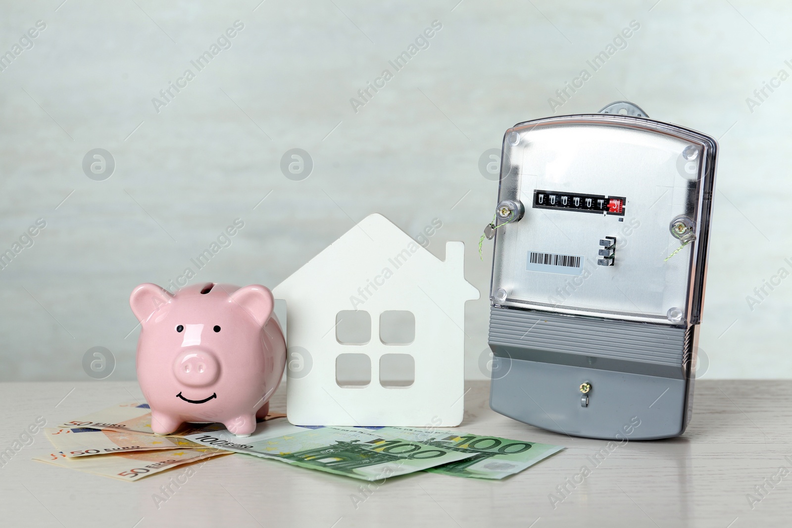 Photo of Electricity meter, piggy bank, house model and euro banknotes on white wooden table