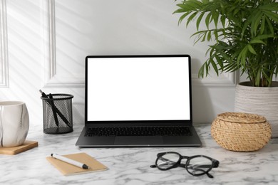 Office workplace with computer, glasses, cup and stationery on marble table near white wall