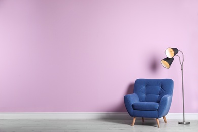 Photo of Comfortable armchair and lamp near color wall with space for text. Interior element