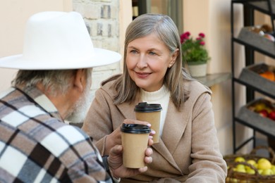 Affectionate senior couple sitting in outdoor cafe and drinking coffee, space for text