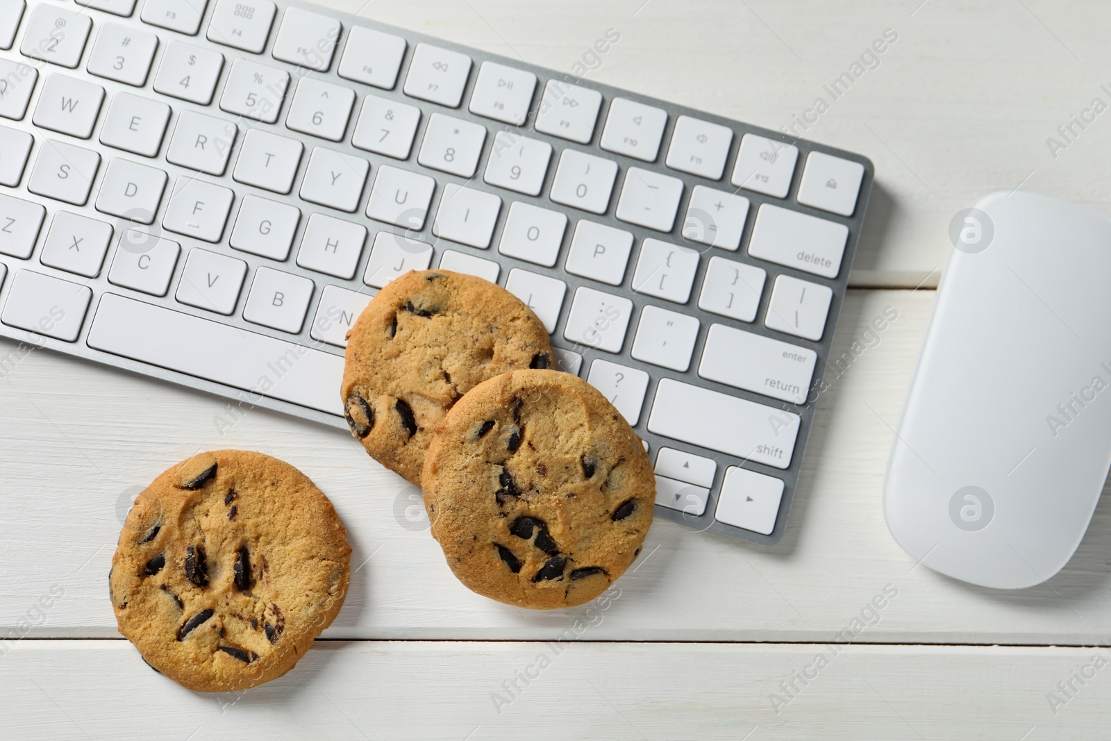 Photo of Chocolate chip cookies, keyboard and computer mouse on white wooden table, flat lay