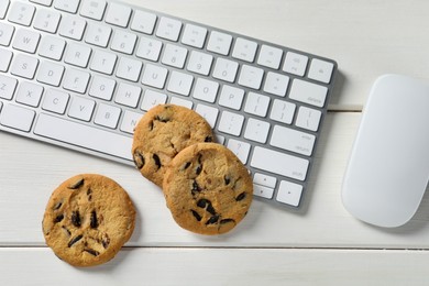 Photo of Chocolate chip cookies, keyboard and computer mouse on white wooden table, flat lay