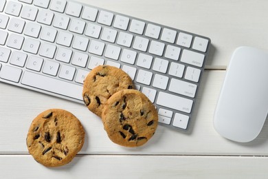 Chocolate chip cookies, keyboard and computer mouse on white wooden table, flat lay