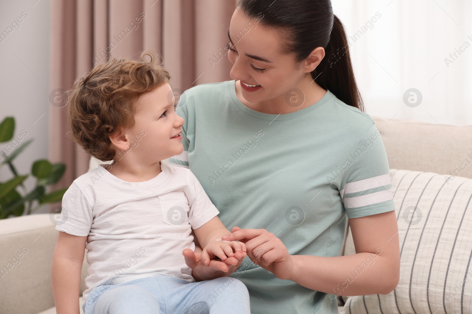 Photo of Mother applying ointment onto her son`s hand on sofa at home