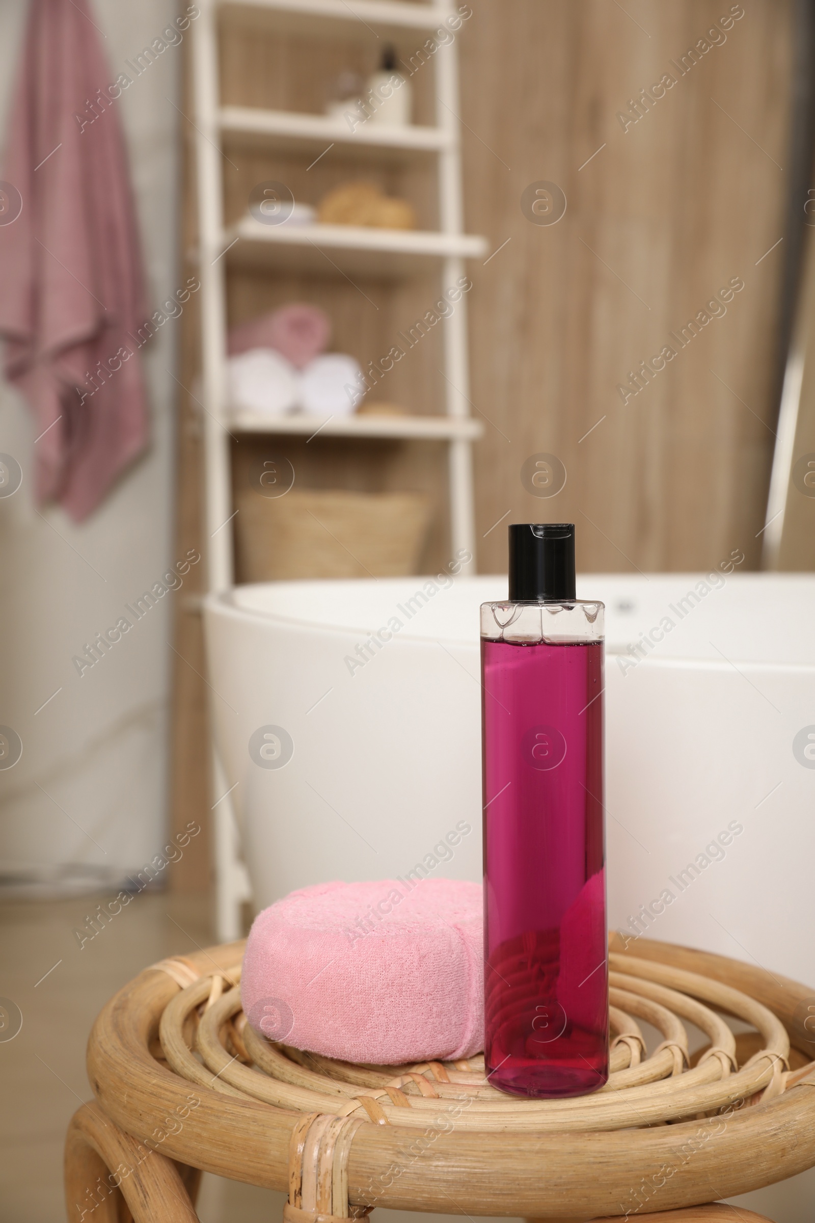 Photo of Bottle of shower gel and sponge on wicker table near tub in bathroom, space for text