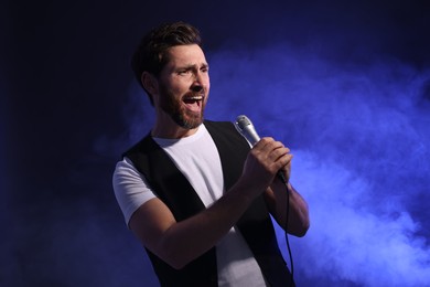 Photo of Handsome man with microphone singing on dark blue background