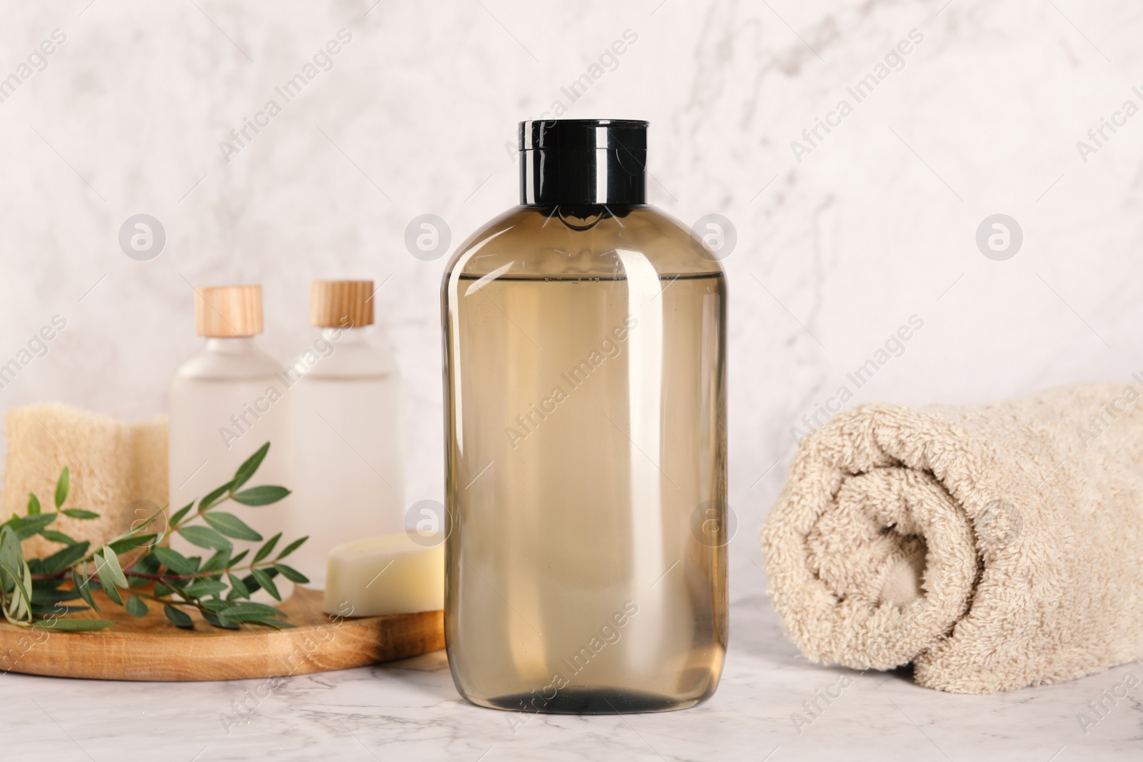 Photo of Shampoo bottle, essential oils, folded towel and loofah on white marble table