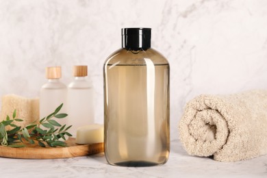 Shampoo bottle, essential oils, folded towel and loofah on white marble table
