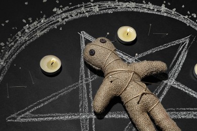 Photo of Voodoo doll pierced with pins and candles in pentagram on table