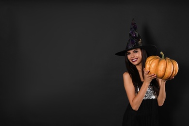 Beautiful woman wearing witch costume with pumpkin for Halloween party on black background, space for text