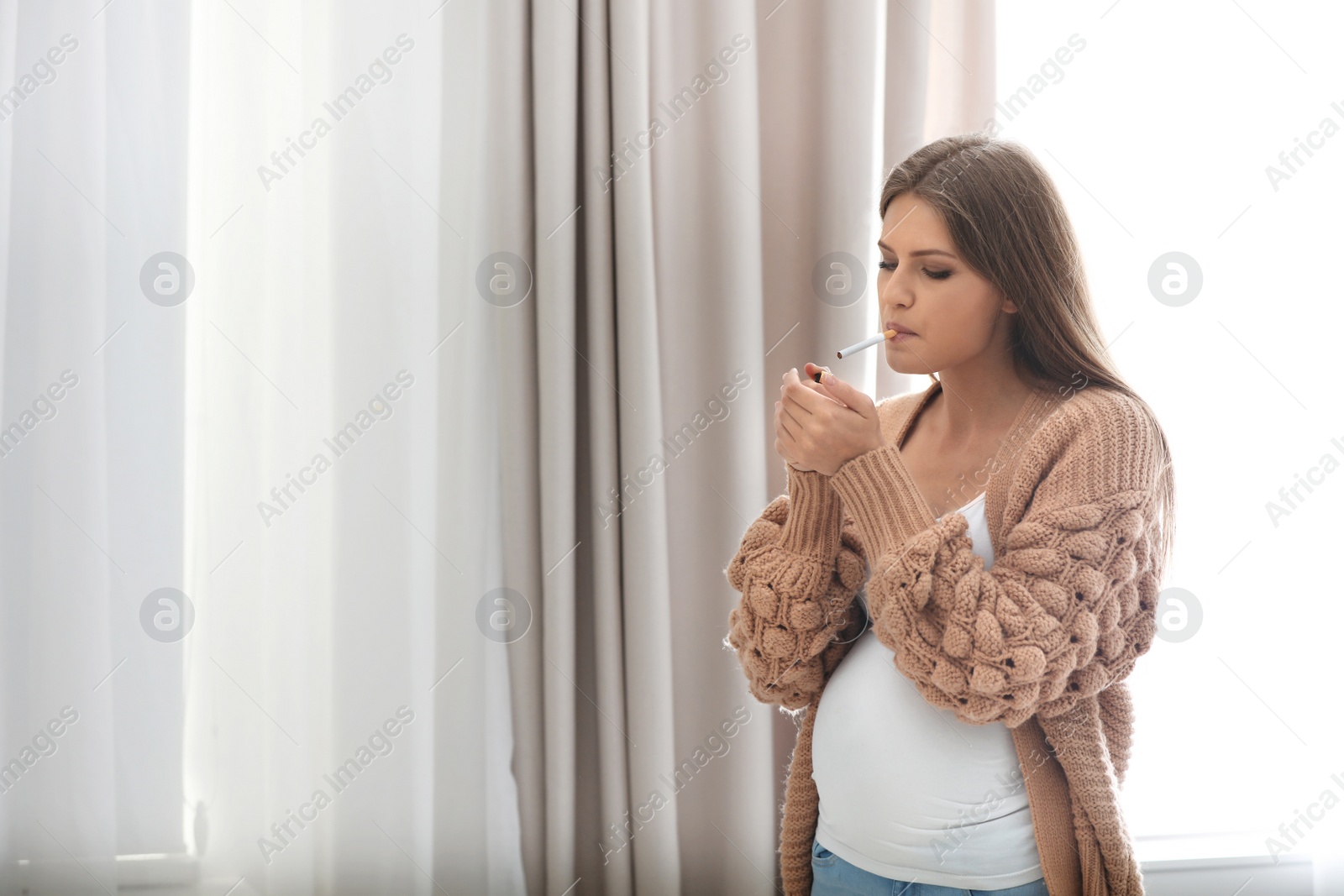 Photo of Young pregnant woman smoking cigarette at home. Harm to unborn baby