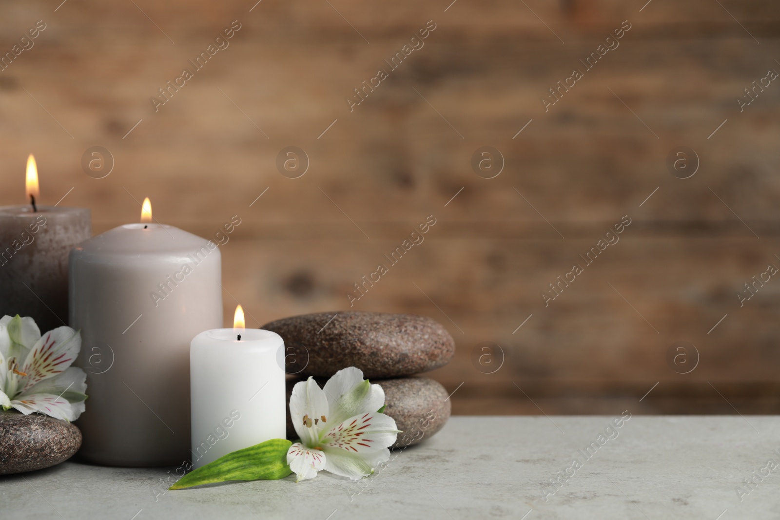 Photo of Beautiful composition with burning candles, spa stones and flowers on light grey table. Space for text