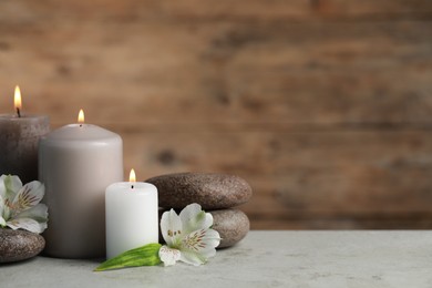 Photo of Beautiful composition with burning candles, spa stones and flowers on light grey table. Space for text